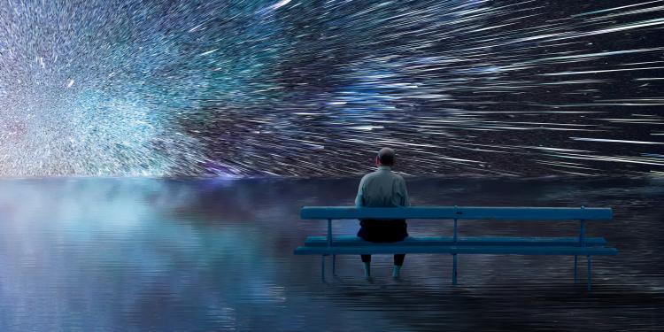 Man sitting on a bench looking at a bright starry environment.